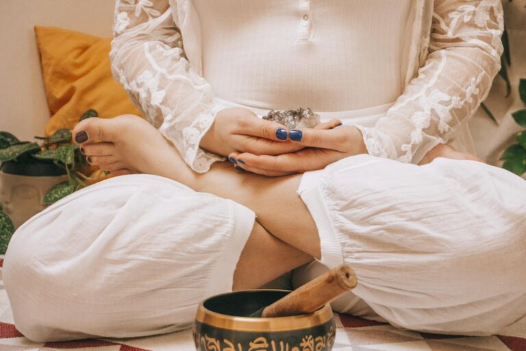 Woman in meditation holding crystal, seated in lotus position with a Tibetan singing bowl, promoting relaxation.